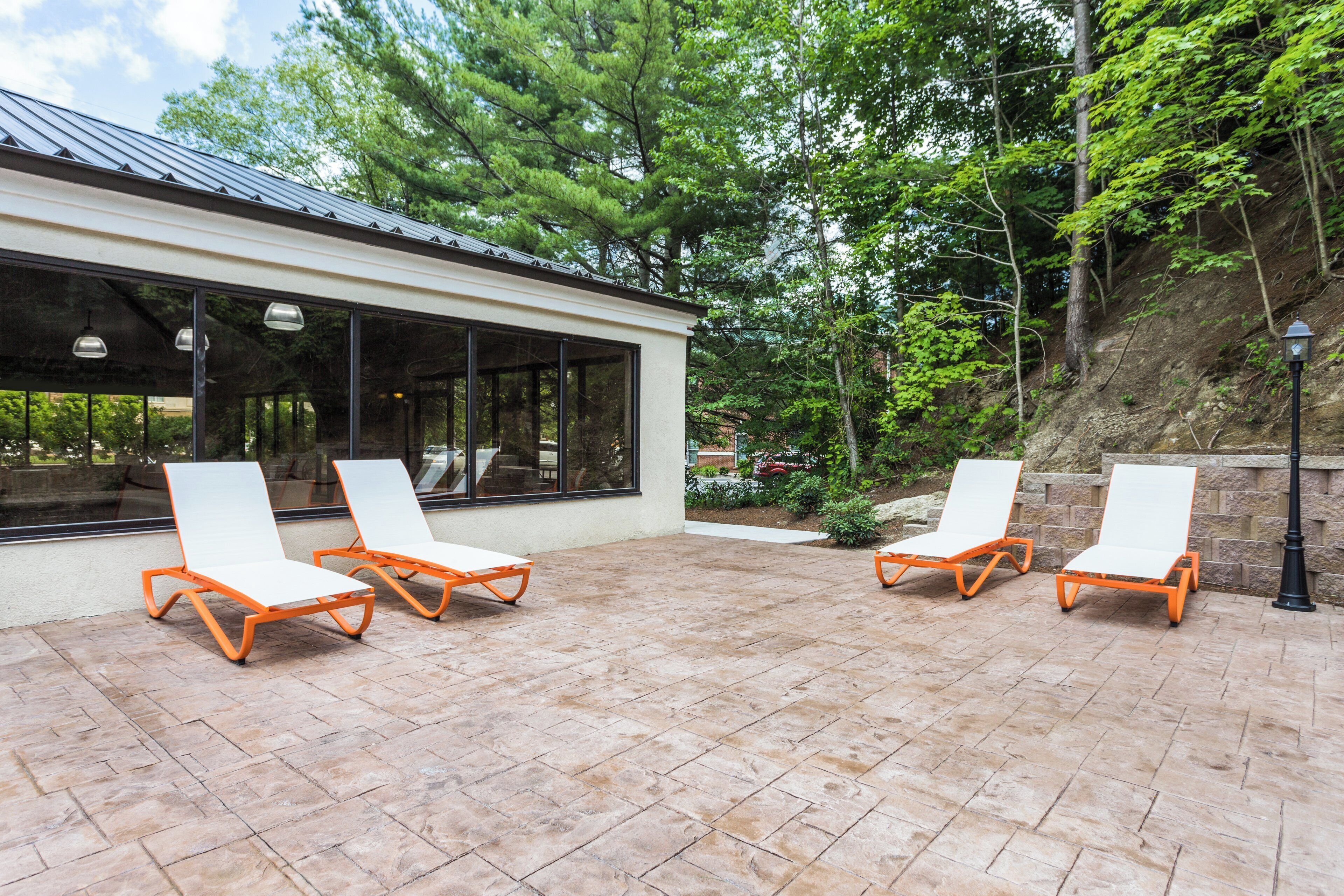 Eine Terrasse mit vier Liegestühlen und einem Gebäude mit großen Fenstern.