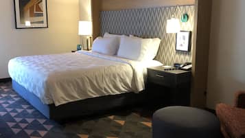 Una habitación de hotel con una cama, mesitas de noche, una lámpara, teléfono y una silla.