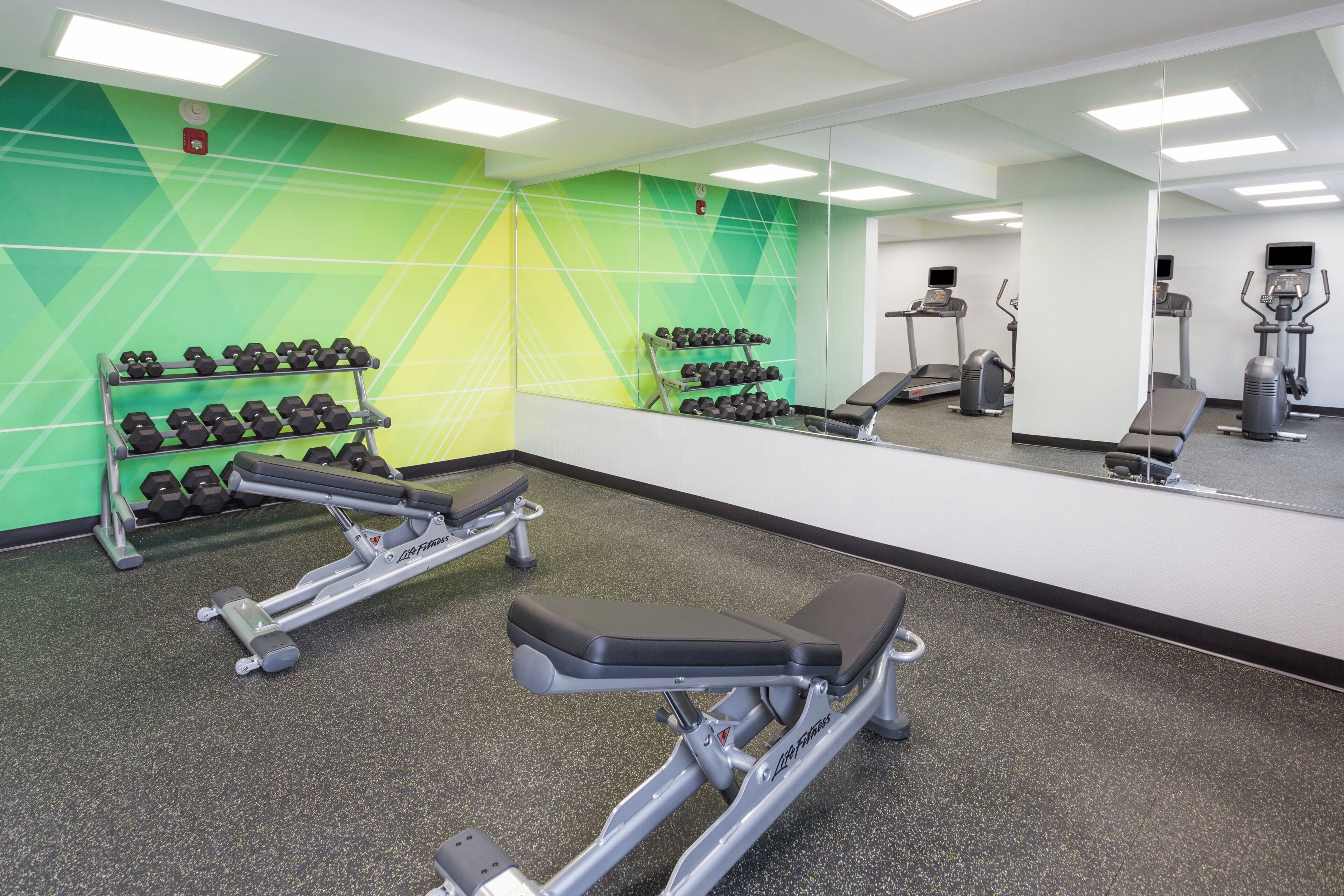 Ein Fitnessraum mit Trainingsgeräten, einer Spiegelwand und Wänden mit grünem Muster.