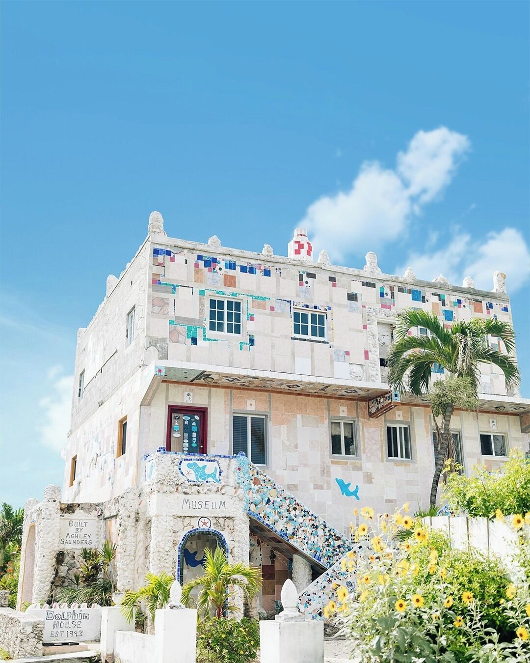 Ein Gebäude mit einer Mosaikfassade, einer roten Tür und einer Treppe, die zum Eingang führt.