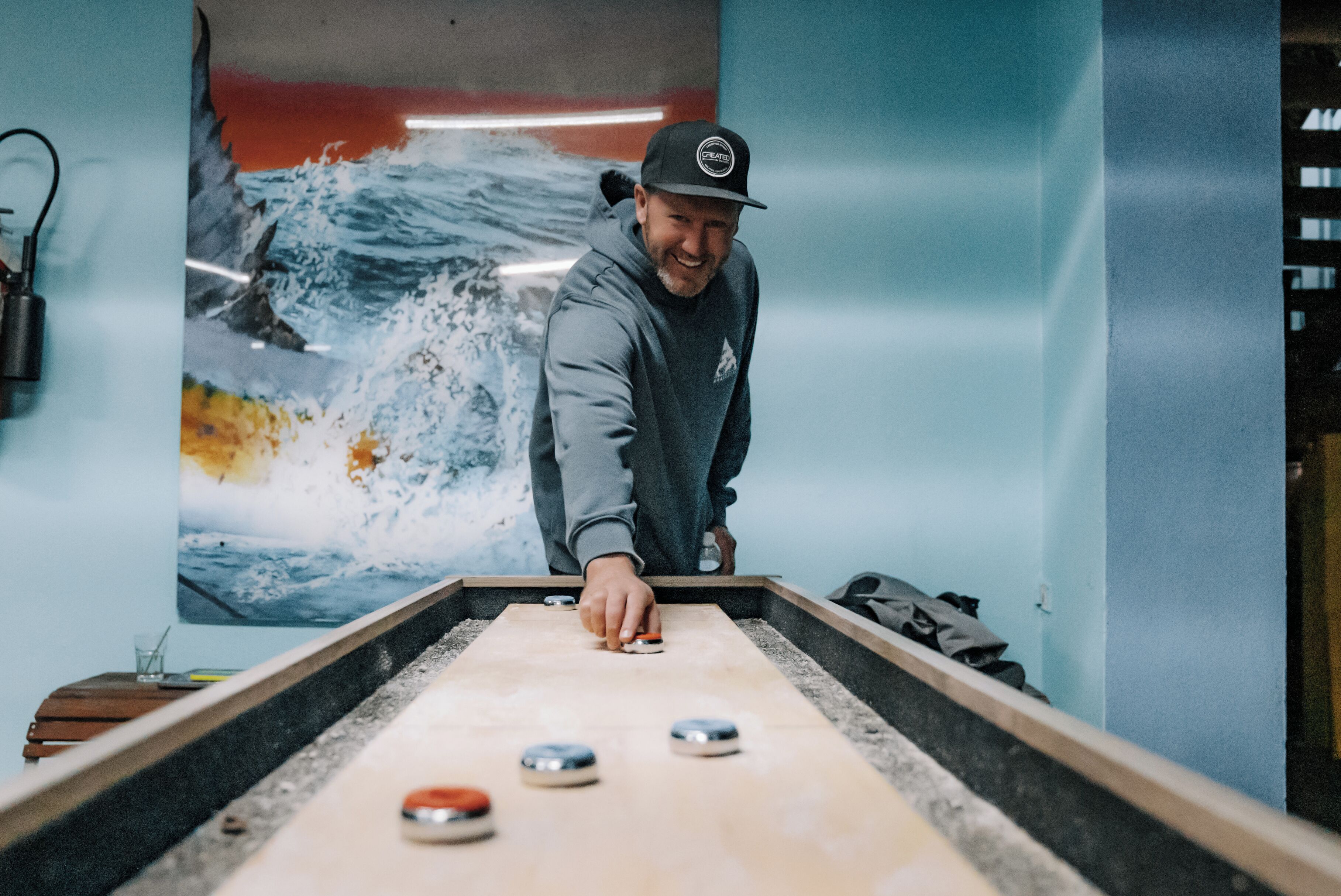 Una persona jugando al juego de bolos en un espacio con un gran mural de una ola en la pared.