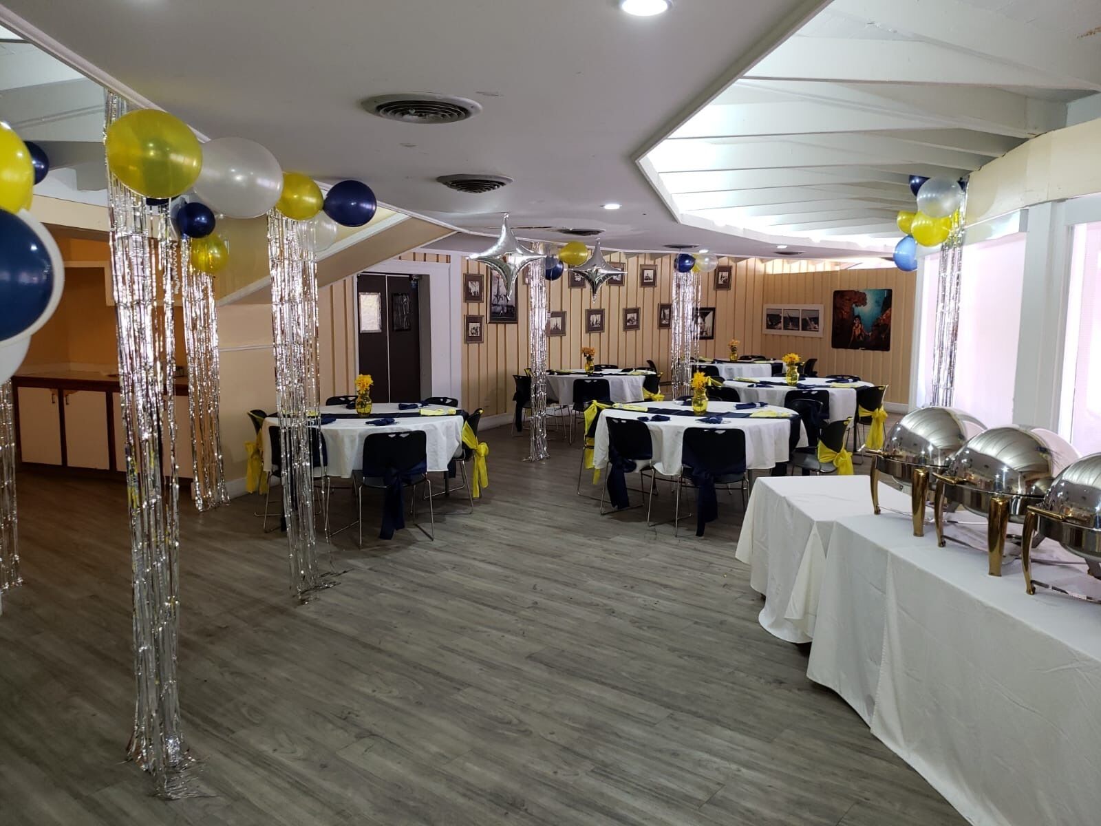 A banquet hall with tables set for a formal event, featuring silver streamers and balloons.