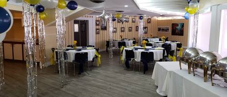 A banquet hall with tables set for a formal event, featuring silver streamers and balloons.