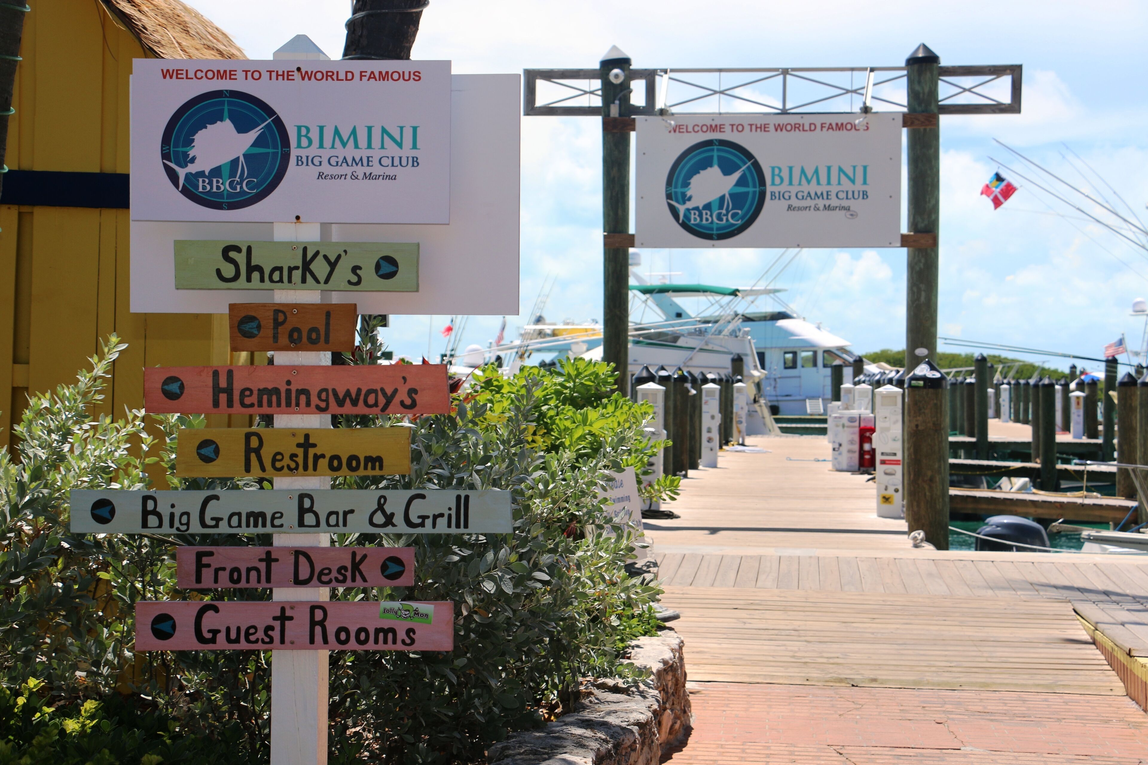 Placa de sinalização com indicações para diversas comodidades, incluindo Big Game Club, piscina, Hemingway's, sanitários, Big Game Bar & Grill, recepção e quartos de hóspedes.