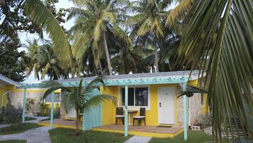 Un edificio pequeño y amarillo con un porche cubierto, rodeado de palmeras.