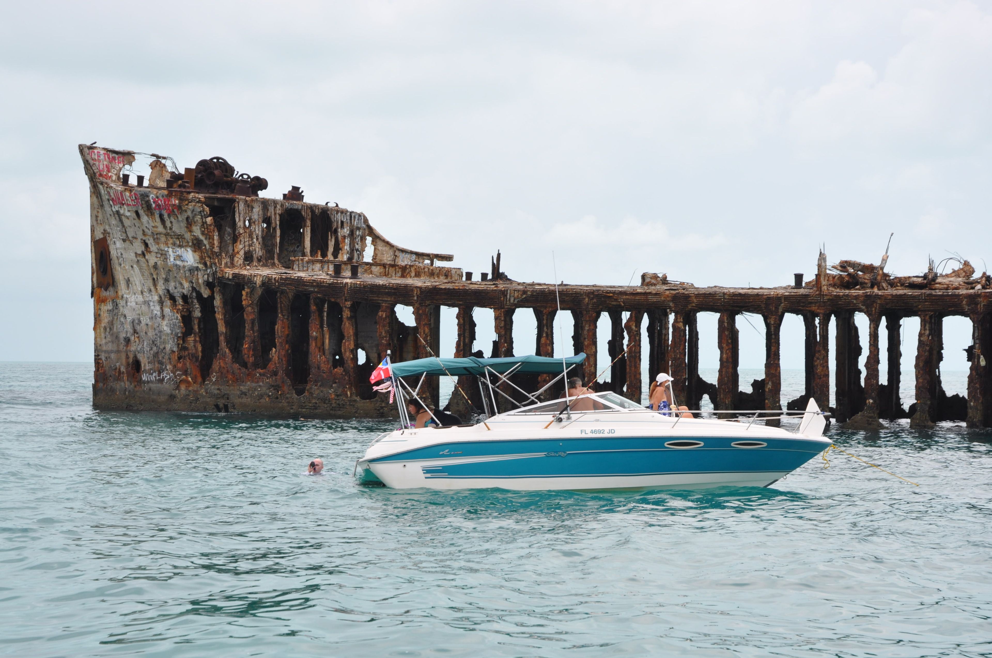 A boat anchored near a rusted pier with a person swimming nearby.