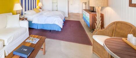 A hotel room with a bed, a sofa, a wooden table, a wicker chair, and a dresser.