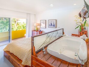 A bedroom with a large bed, a bathtub, a balcony with yellow walls, and a view of greenery. - Bimini Big Game Club Resort & Marina (Alice Town)