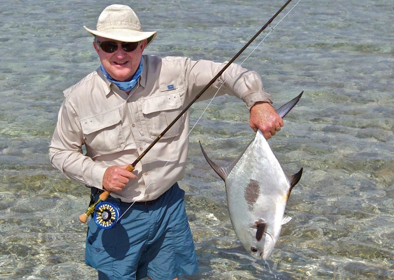 Una persona sosteniendo un pez en agua clara y poco profunda.