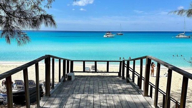A wooden deck leading to a beach with clear turquoise water, boats, and a sandy shore. - Bimini Big Game Club Resort & Marina (Alice Town)