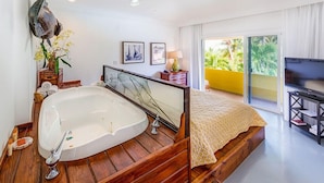 A modern hotel room with a large bathtub, a bed with a yellow patterned bedspread, a television on a black stand, and a balcony with a yellow railing. - Bimini Big Game Club Resort & Marina (Alice Town)