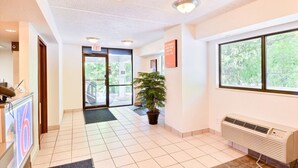 Een hotel lobby met een receptiebalie, een grote potplant, een raam met uitzicht op bomen en een plafond met inbouwspots.