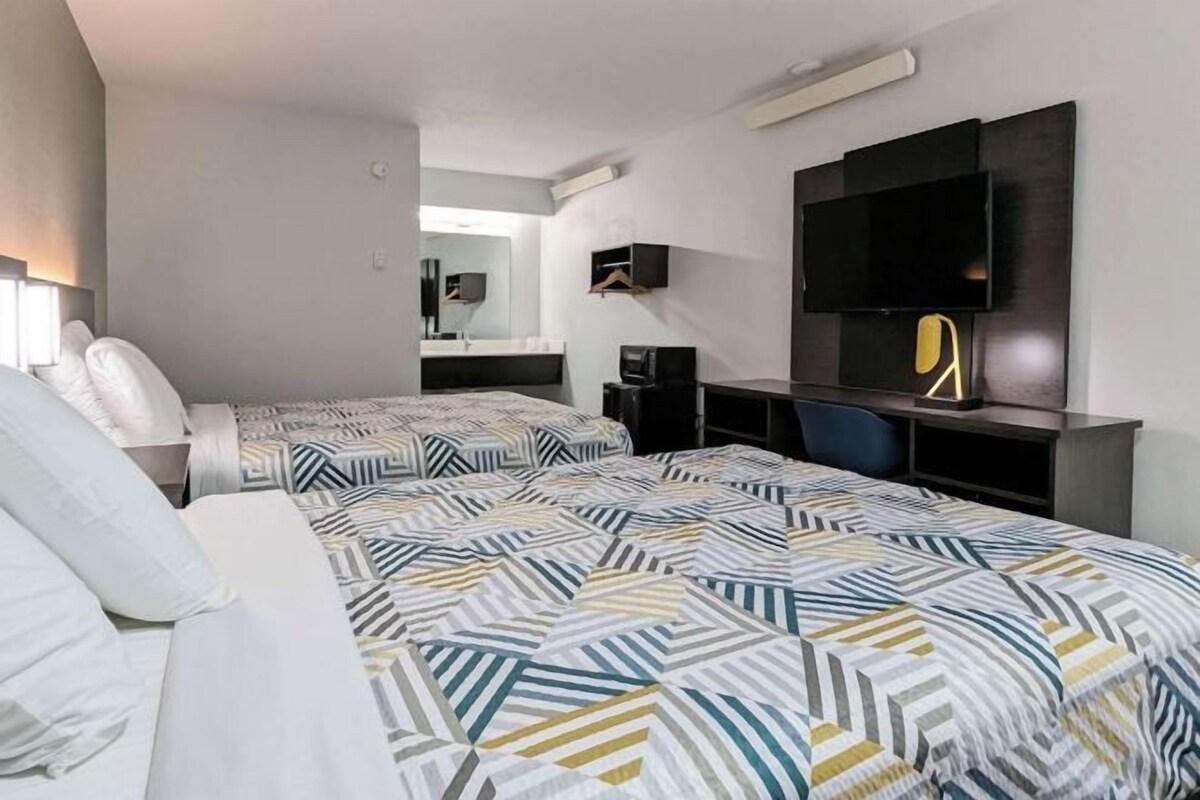 A modern hotel room with two beds, a desk, a chair, a flat-screen TV, and a mirror.