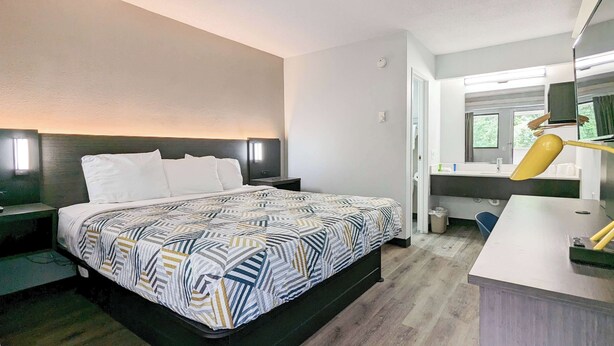 Een hotelkamer met een bed, nachtkastjes, een bureau met lamp, een spiegel en een raam.