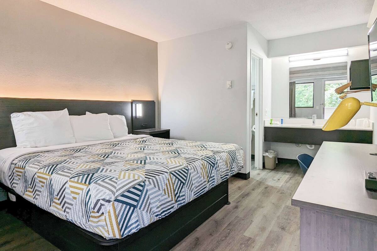 A hotel room with a bed, bedside tables, a desk with a lamp, a mirror, and a window.