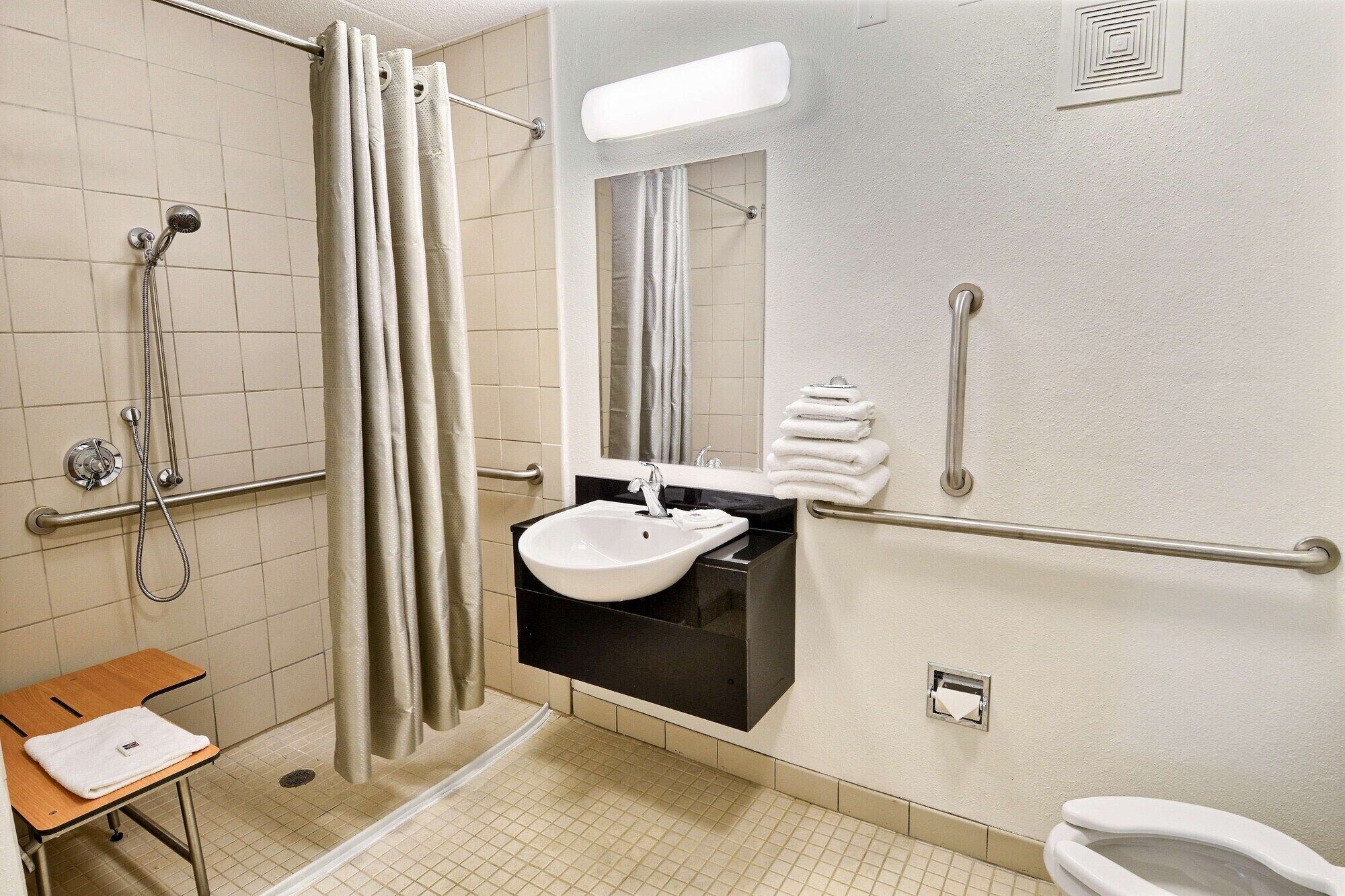 A bathroom with a shower, sink, toilet, and grab bars.
