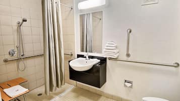 A bathroom with a shower, sink, toilet, and grab bars.