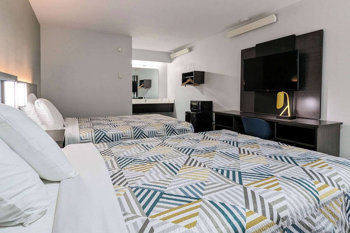 A hotel room with a large bed, a TV, a desk, and a mirror.