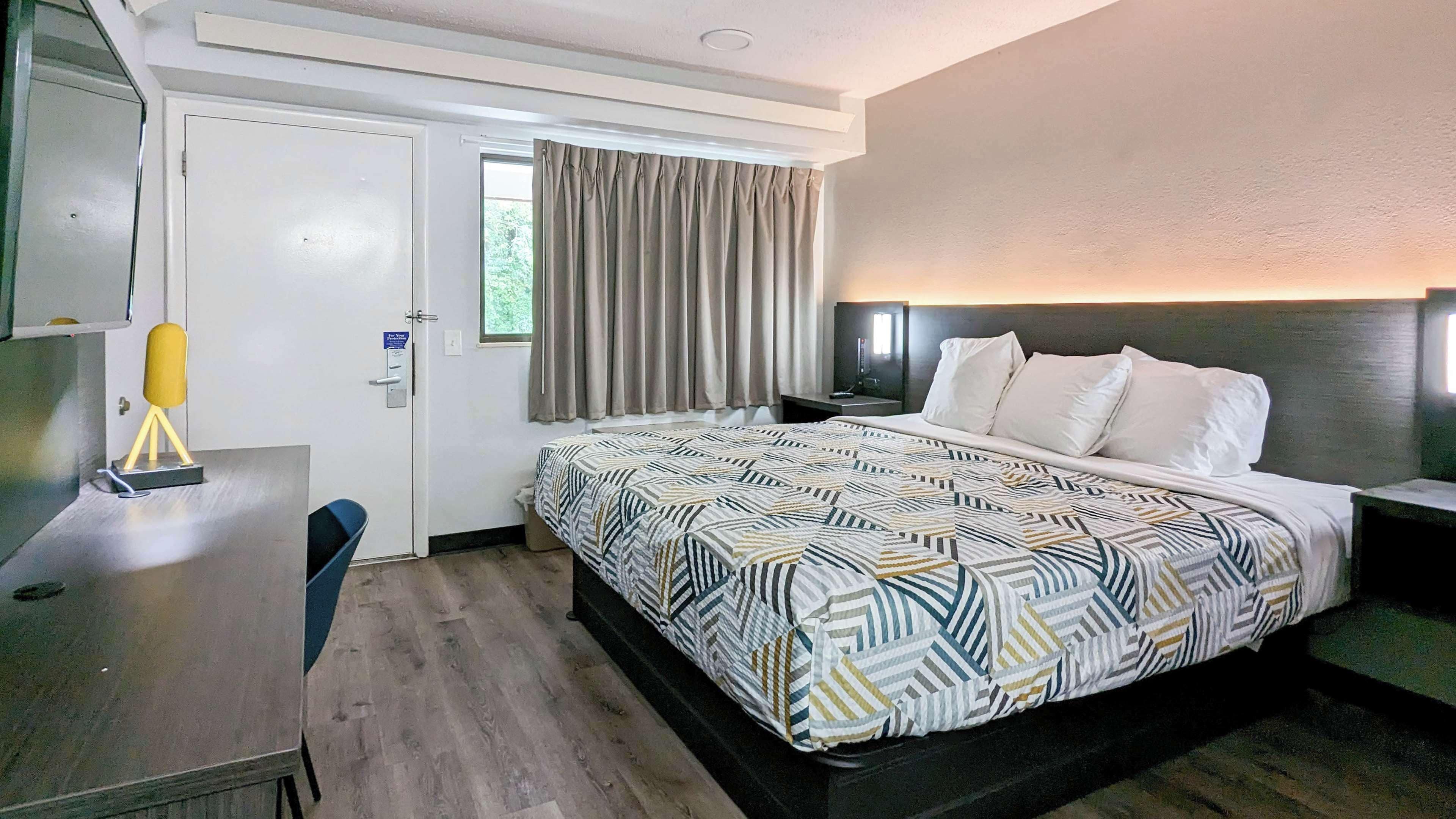 A hotel room with a bed, a desk, a chair, a TV, and a window with curtains.