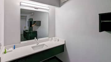A bathroom with a white sink, a large mirror, and a green countertop.