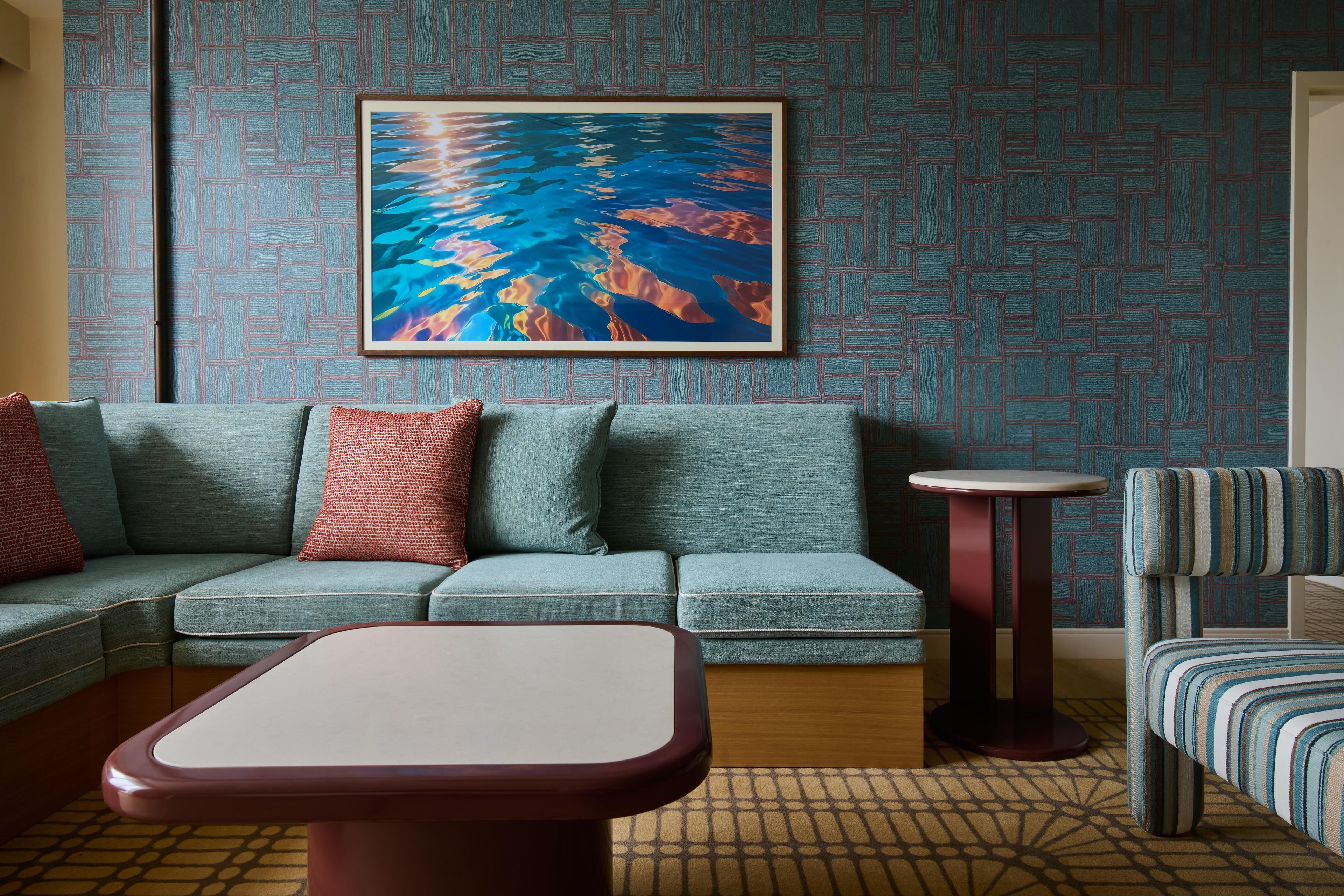 A room with a sofa, a small round table, a striped armchair, and a painting on the wall.