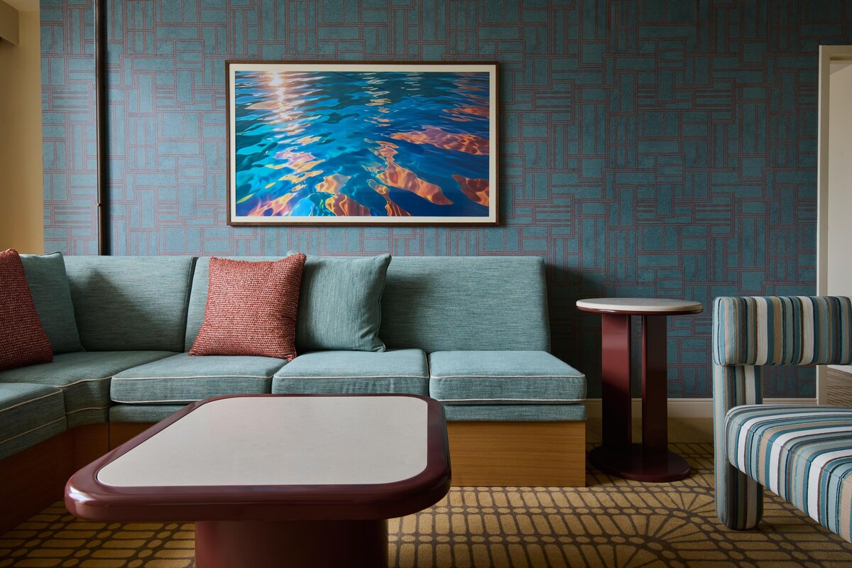 Una habitación con un sofá, una mesita redonda pequeña, un sillón a rayas y un cuadro en la pared.