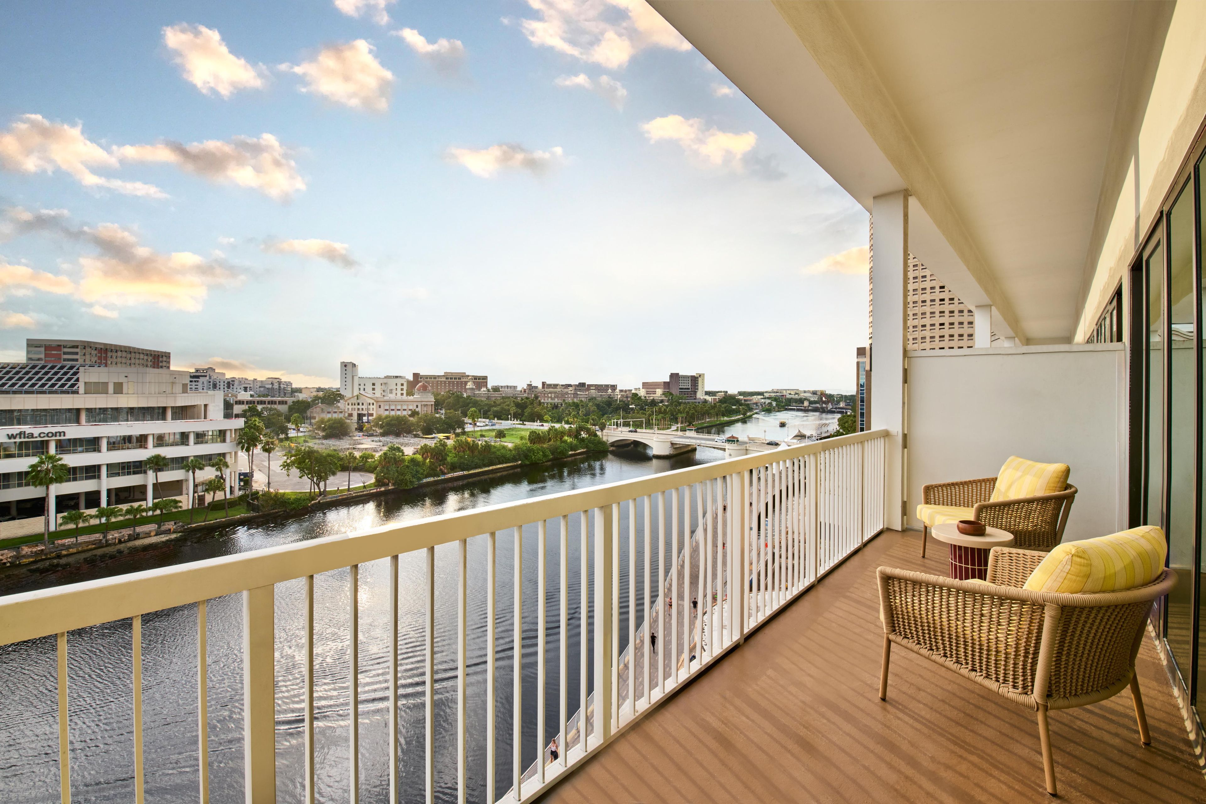 Ein Balkon mit Korbmöbeln, Blick auf einen Fluss und Gebäude im Hintergrund.