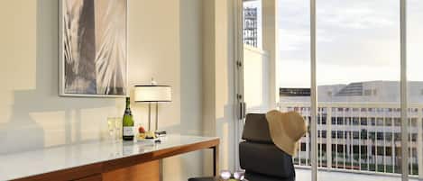 Una habitación de hotel con un escritorio, una silla, un ventanal con vistas a edificios y un cuadro en la pared.