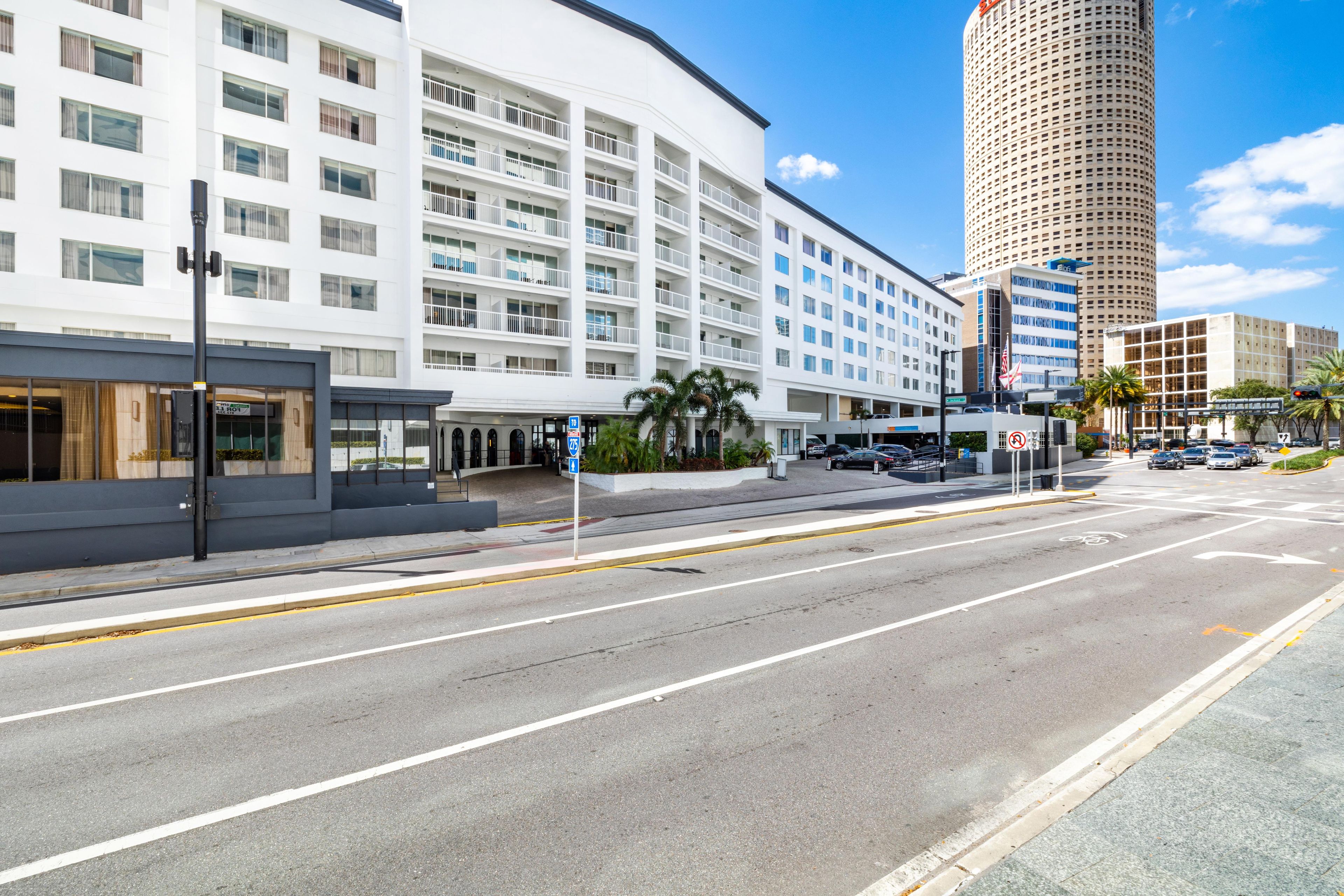 A modern hotel with a curved facade, multiple balconies, and a parking area in front.