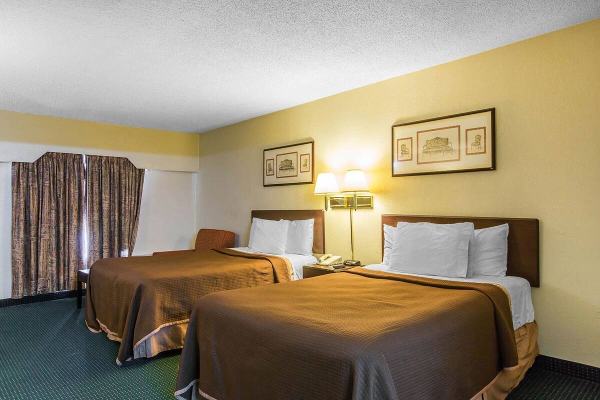 A hotel room with two beds, a nightstand with a lamp, a telephone, and framed pictures on the wall.
