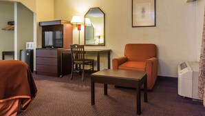 Ein Hotelzimmer mit einem Bett, einem Schreibtisch mit Stuhl, einem Fernseher, einem Spiegel, einem gerahmten Bild an der Wand und einem Drucker.