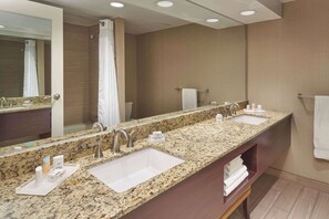 Ein Badezimmer in einem Hotel mit einer Granit-Arbeitsplatte, zwei Waschbecken, einem großen Spiegel und einer Duschkabine.