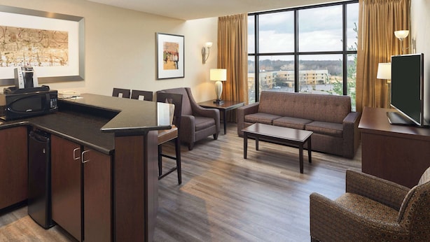 Une chambre d’hôtel avec un coin repas, un canapé, une télévision et une vue sur la ville.