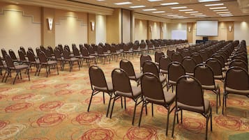 A conference room with rows of chairs, a carpeted floor, and a projector screen.