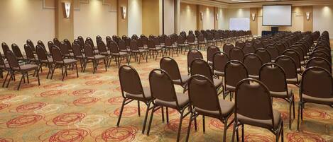 A conference room with rows of chairs, a carpeted floor, and a projector screen.