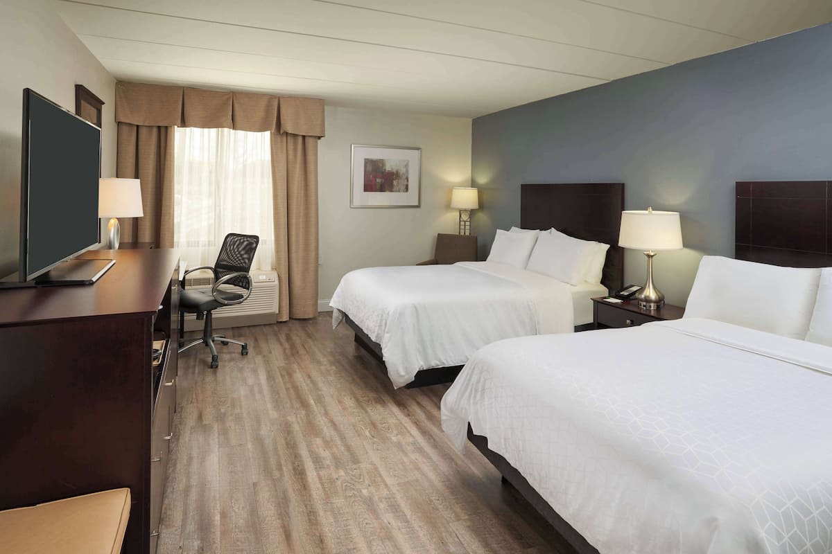 Una habitación de hotel con dos camas, un escritorio, una silla y un televisor.