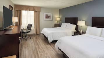 A hotel room with two beds, a desk, a chair, and a television.