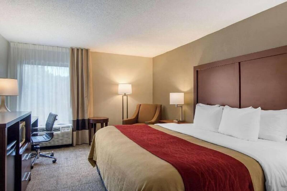 A hotel room with a large bed, two bedside lamps, a desk with a chair, and a window with curtains.
