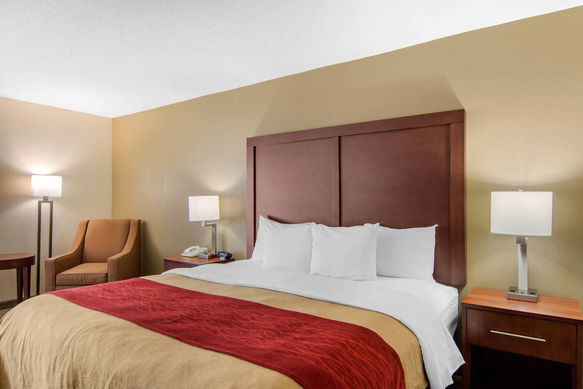 A hotel room with a large bed, a chair, a desk, and two bedside lamps.