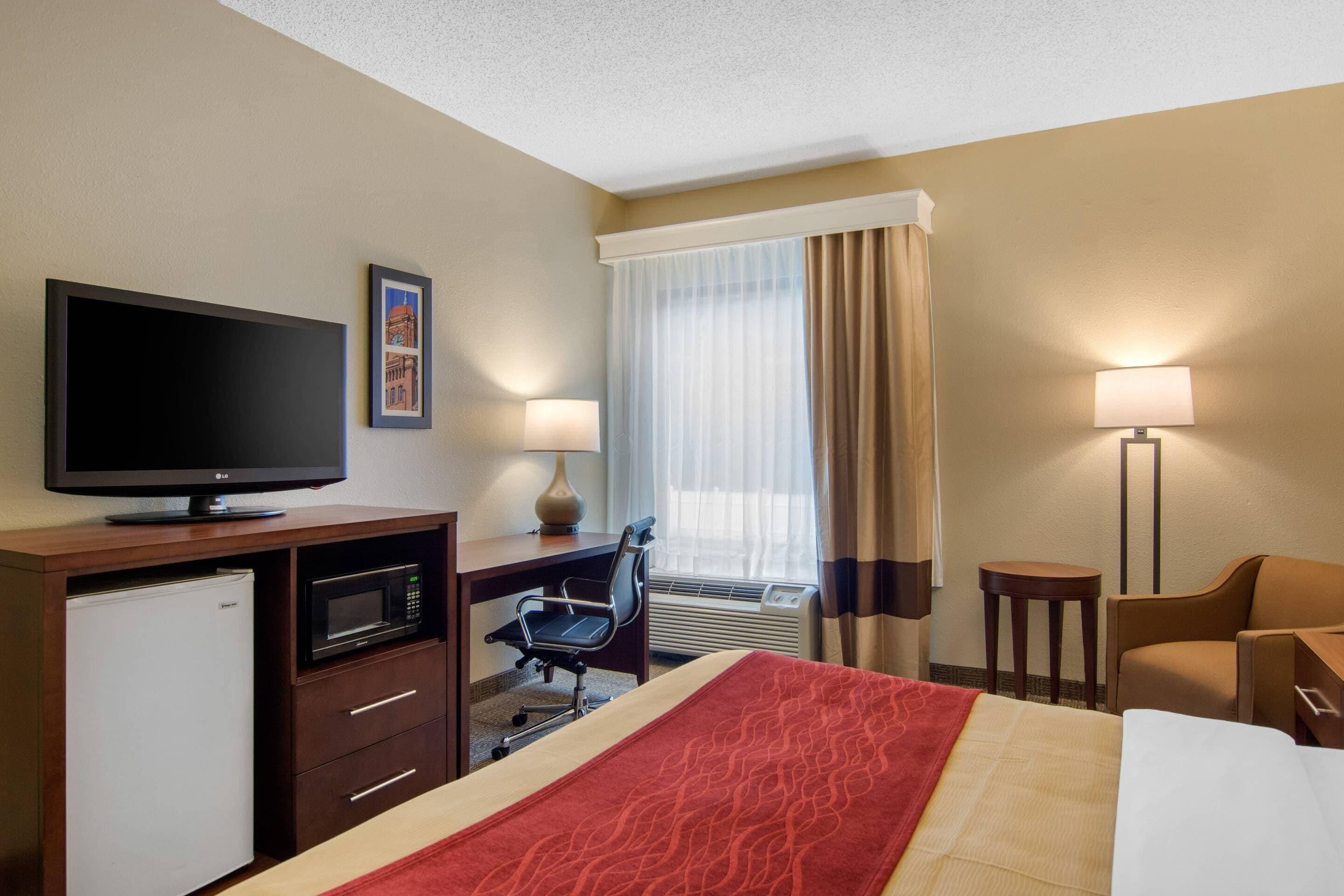 A hotel room with a bed, a desk with a computer, a television, a microwave, and a small refrigerator.