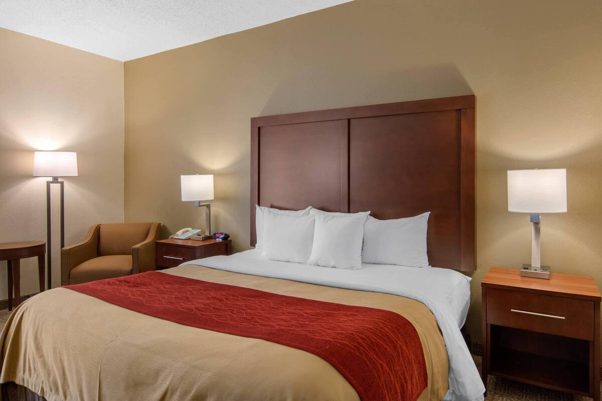 A hotel room with a large bed, two bedside tables, a chair, and a nightstand with a lamp.