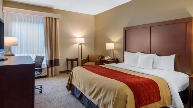 A hotel room with a large bed, a desk with a lamp, a chair, a small table, and a telephone. - Comfort Inn Chester - Richmond South (Chester)