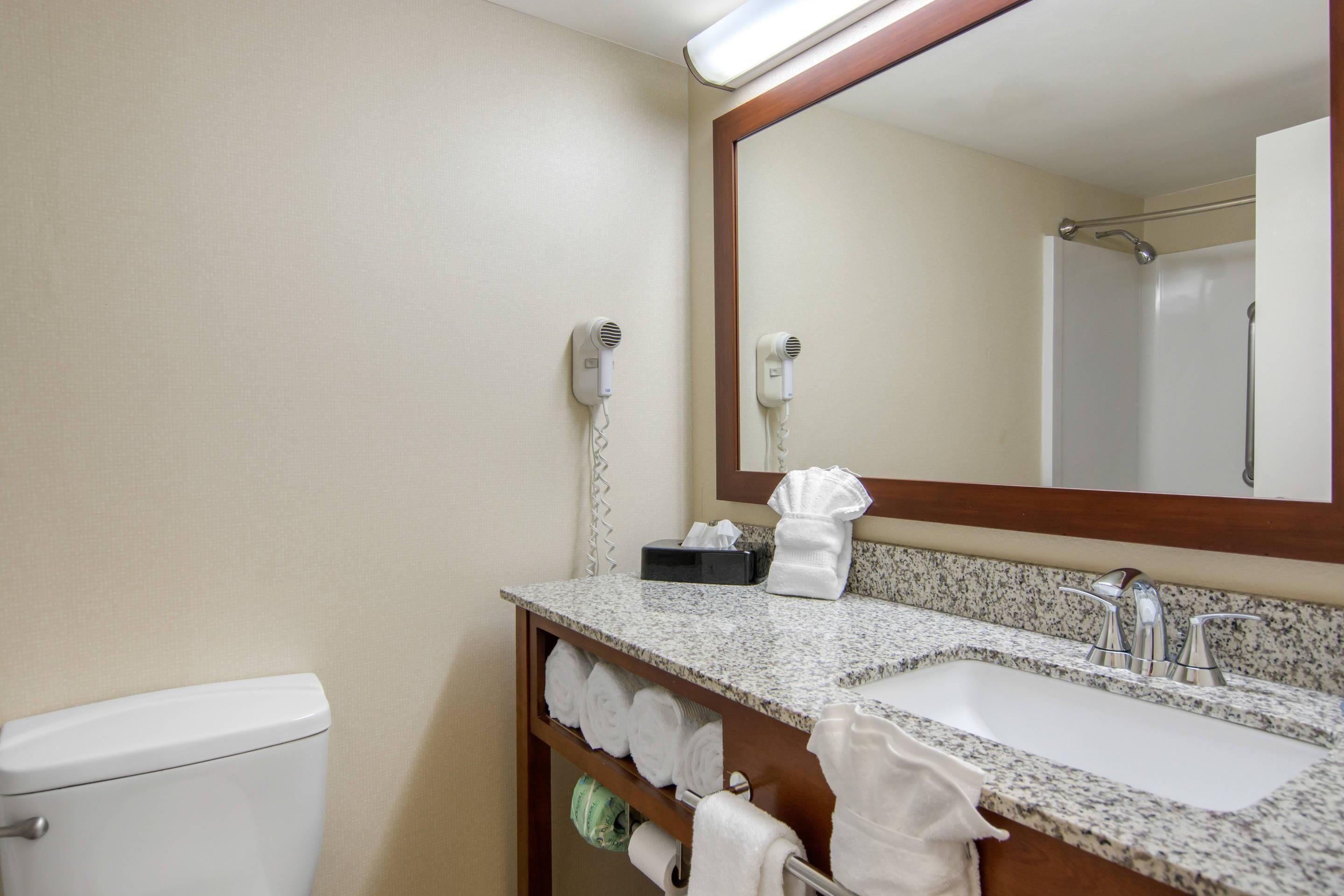 A bathroom with a toilet, sink, and two hair dryers mounted on the wall.