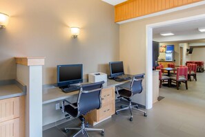 A modern hotel room with a desk, two monitors, a keyboard, and a chair. There is a dining area with tables and chairs in the background. - Comfort Inn Chester - Richmond South (Chester)