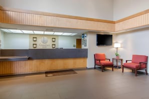 A hotel reception area with a wooden reception desk, a flat-screen TV, and two red chairs. - Comfort Inn Chester - Richmond South (Chester)