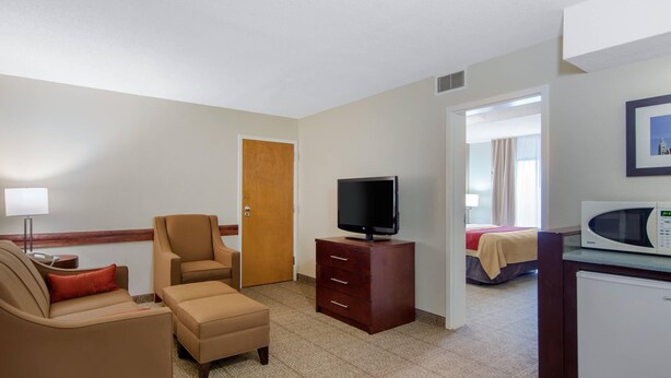 A hotel room with a sofa, armchair, TV, dresser, microwave, and a bed in the background.