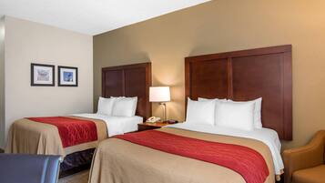 A hotel room with two beds, a desk with a lamp, a chair, and framed pictures on the wall.