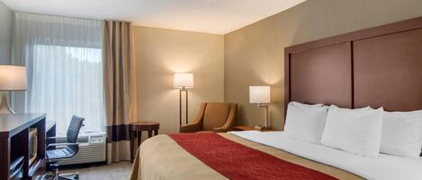 Een hotelkamer met een groot bed, een bureau met stoel, een lamp en een raam met gordijnen.