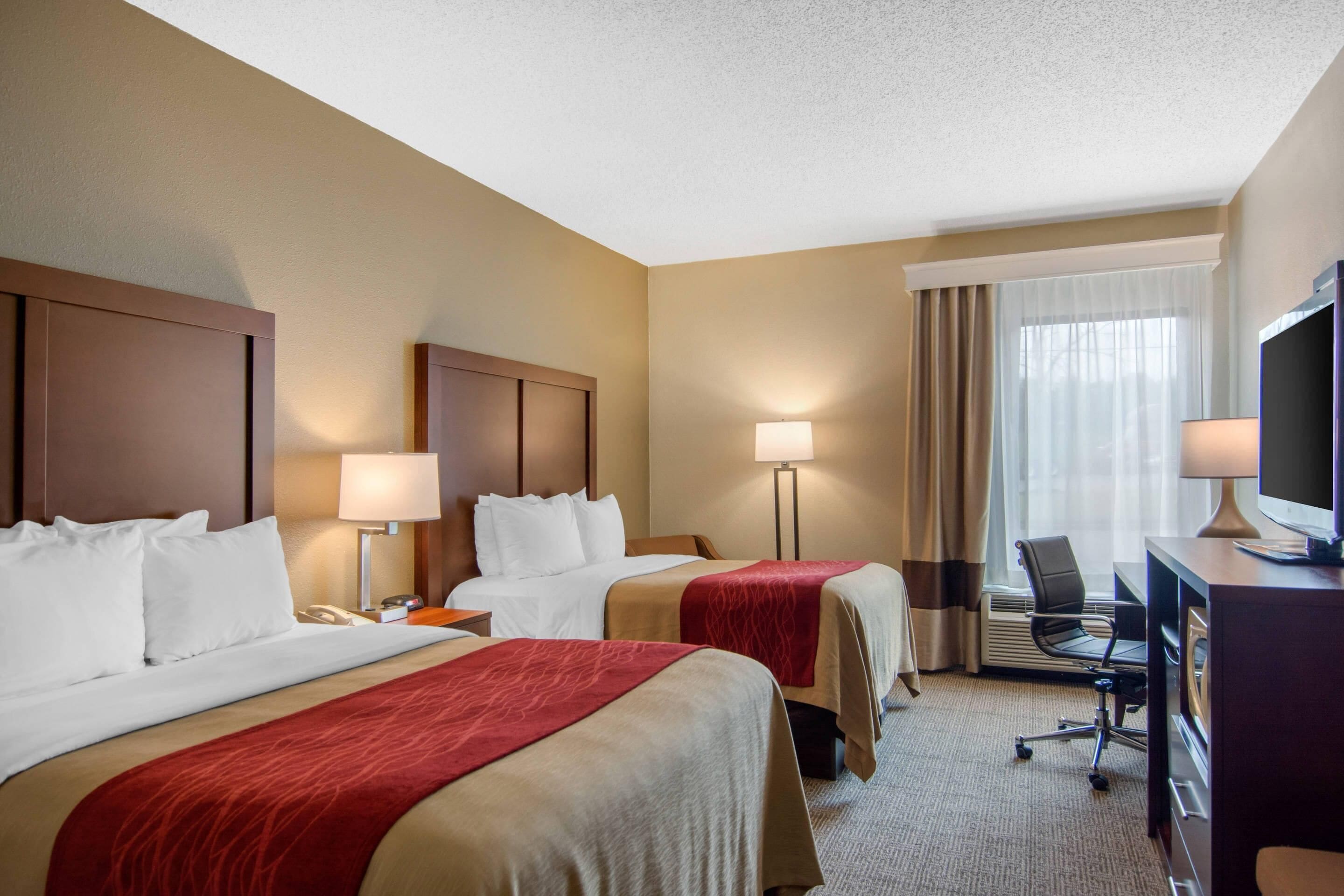 A hotel room with two beds, a desk with a computer, a chair, and a TV.
