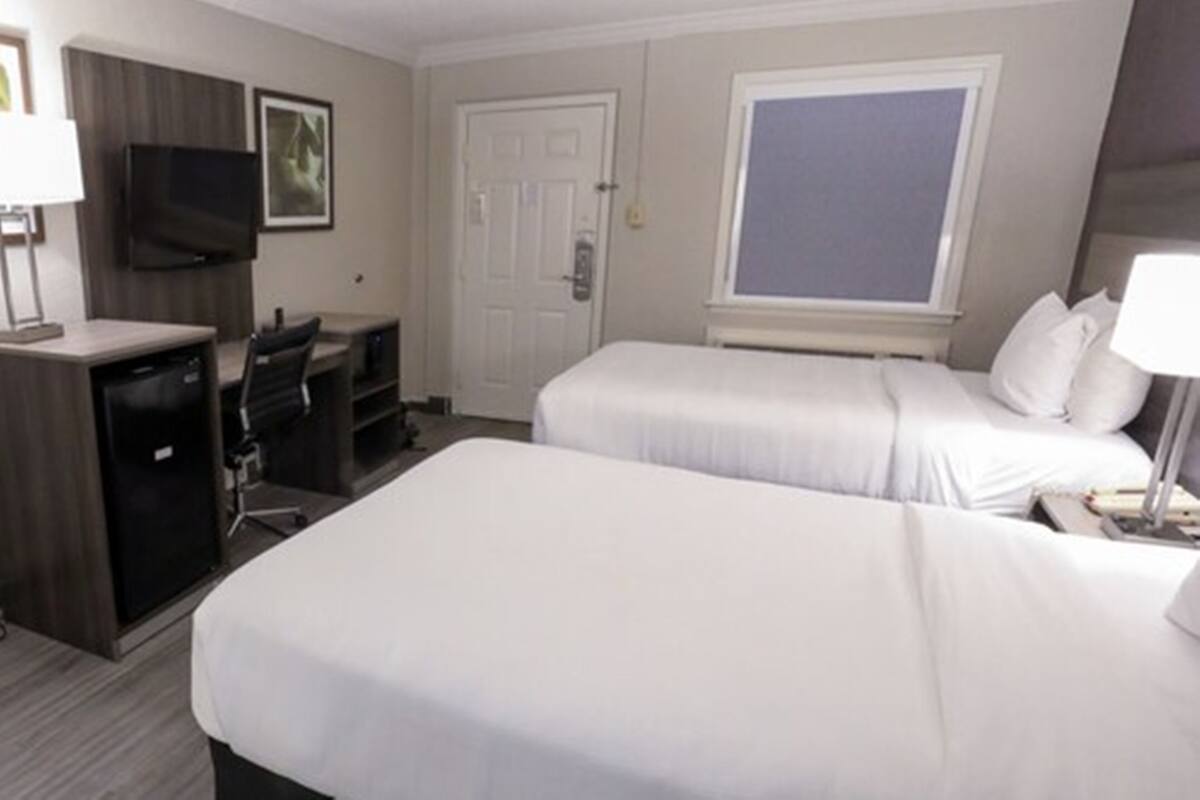 A hotel room with two beds, a desk with a chair, a television, and a window.